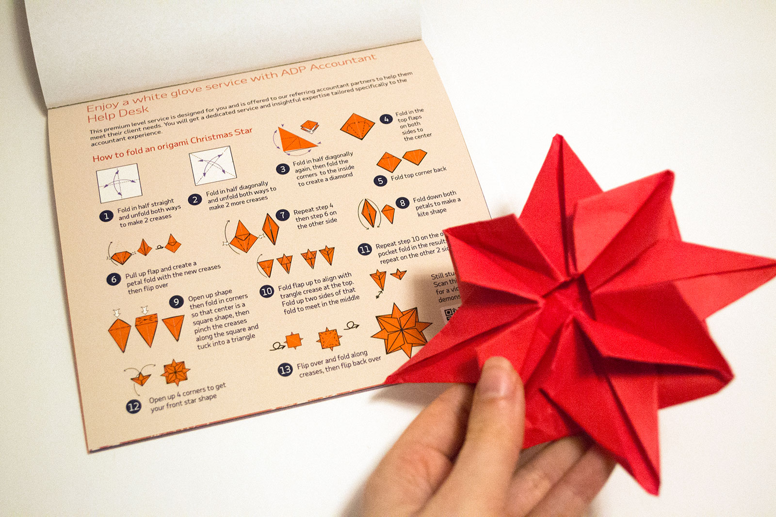 inside page of instructions for how to fold a christmas star with me holding a folded one out of focus beside the page.