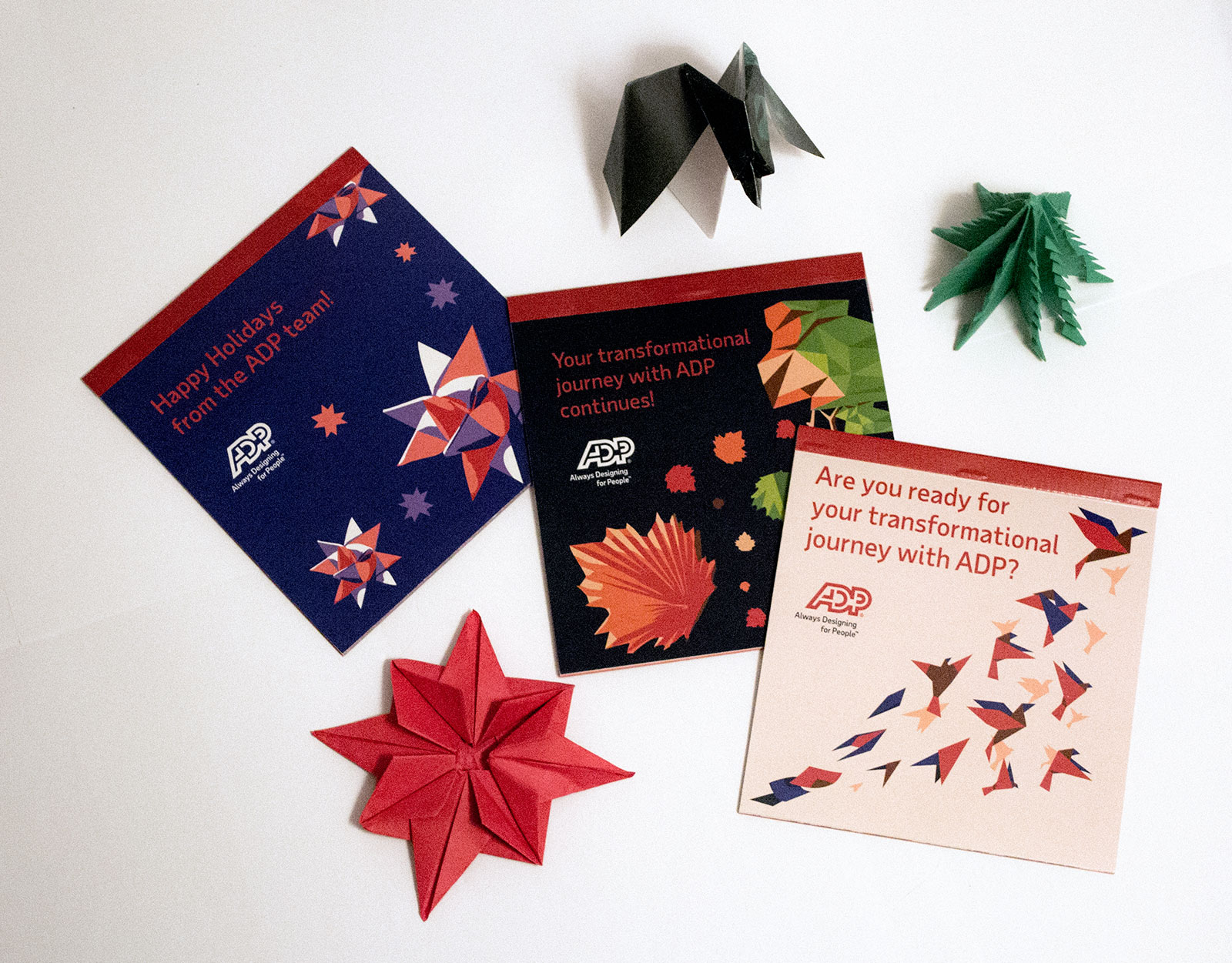 3 Origami booklets arranged with origami folded pieces together. The first book title reads Happy Holidays from the ADP team! the second reads Your transformational journey with ADP continues! and the 3rd reads Are you ready for your transformational journey with ADP?